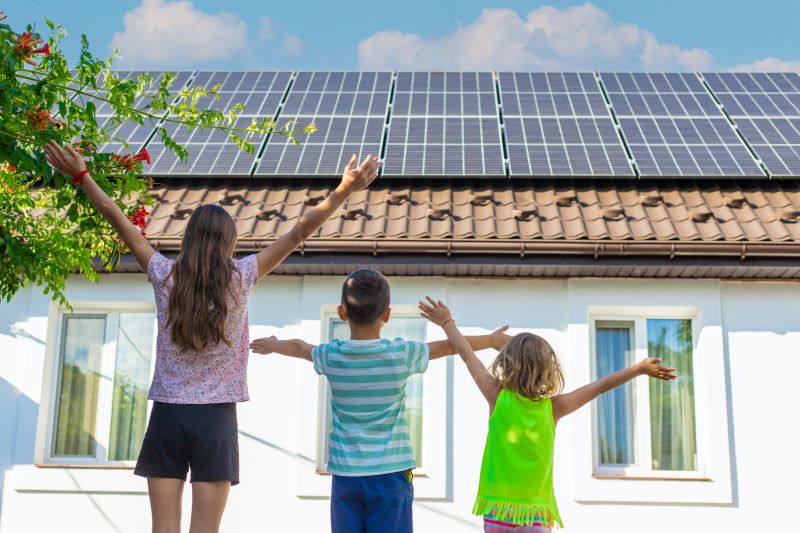 Tre bambini a braccia aperte davanti a una casa con i pannelli sul tetto