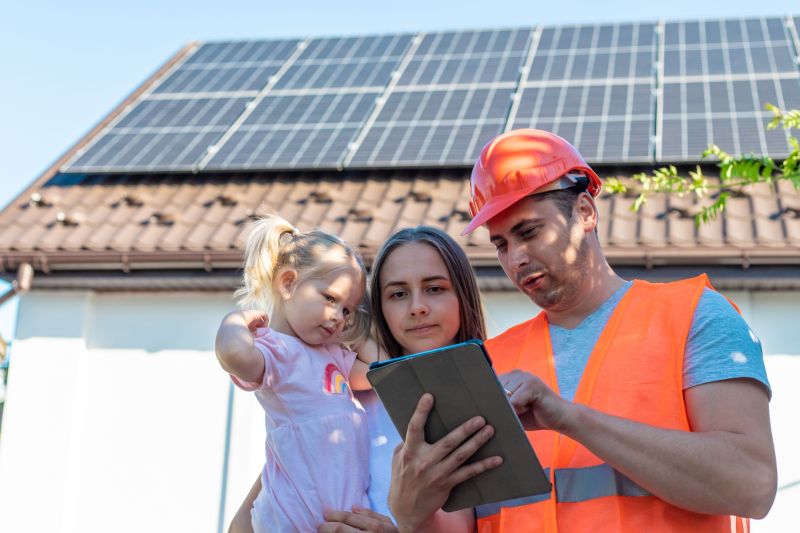 Un tecnico mostra a una famiglia i dati dell’impianto sul tablet, davanti alla casa con i pannelli